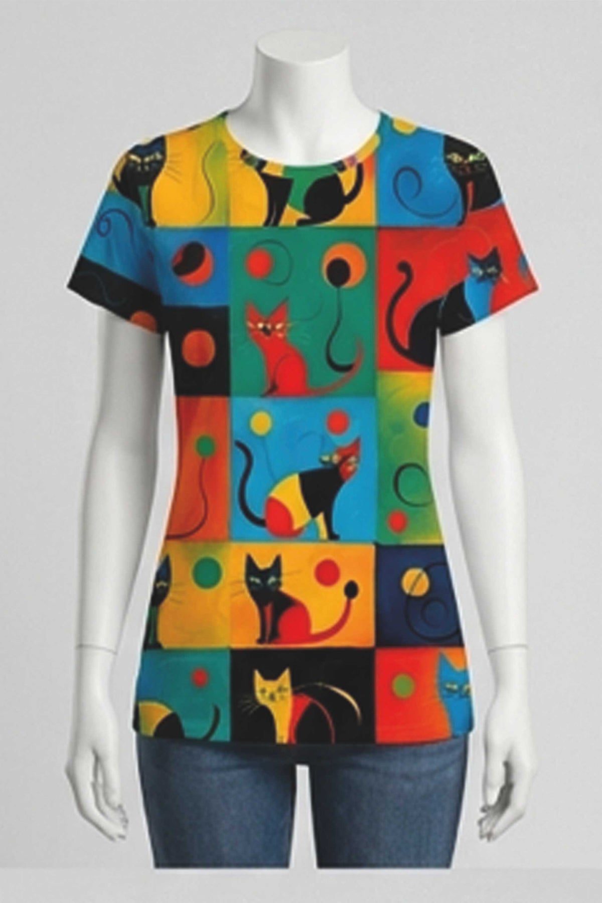 A multicolor short-sleeve t-shirt with a playful patchwork pattern of black cats, colorful circles, and geometric blocks, displayed on a white mannequin torso with blue jeans against a light gray background.
