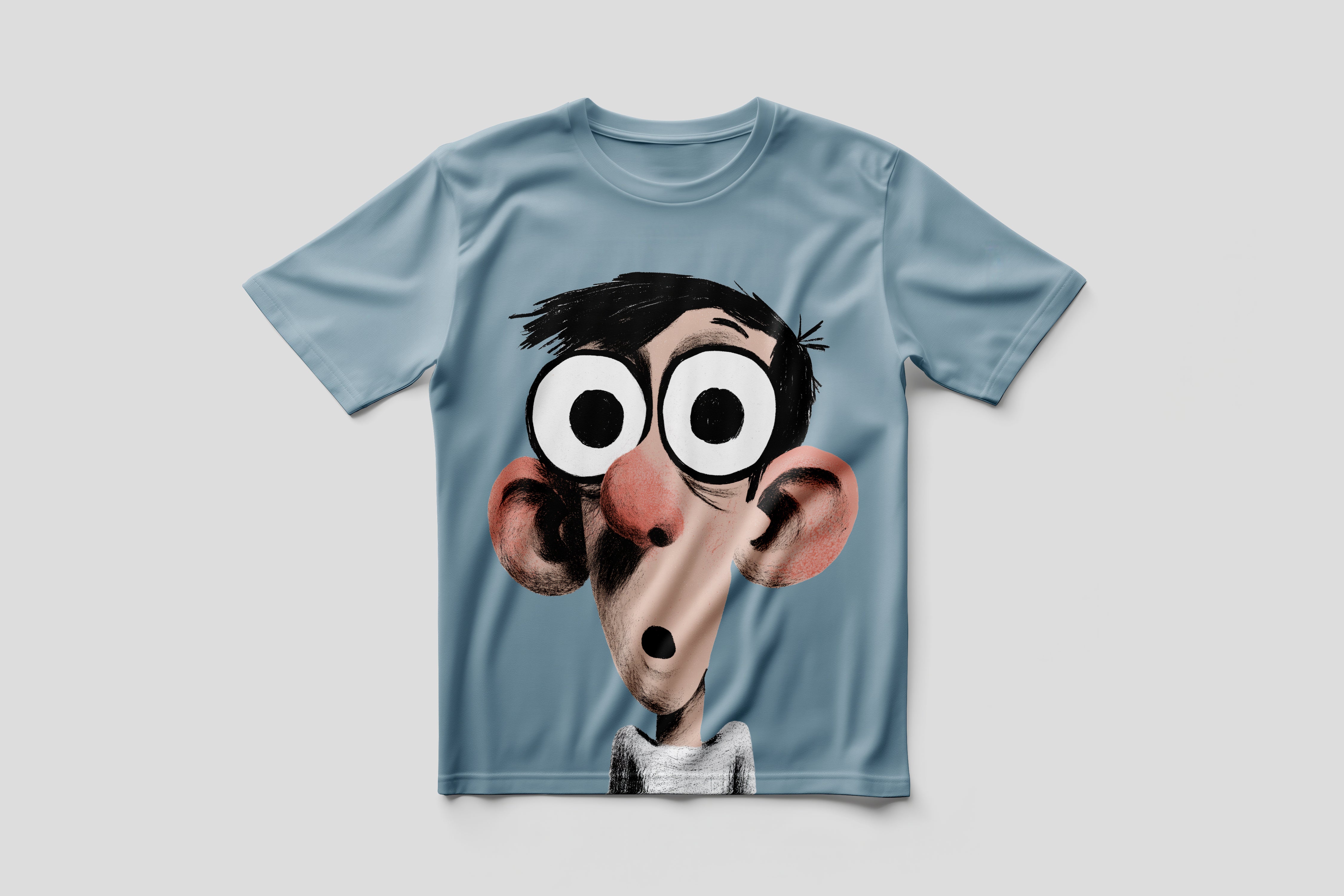 A light blue short-sleeve t-shirt featuring a large graphic print of a cartoon character with oversized eyes, black hair, and a pinkish nose, displayed against a neutral gray background.