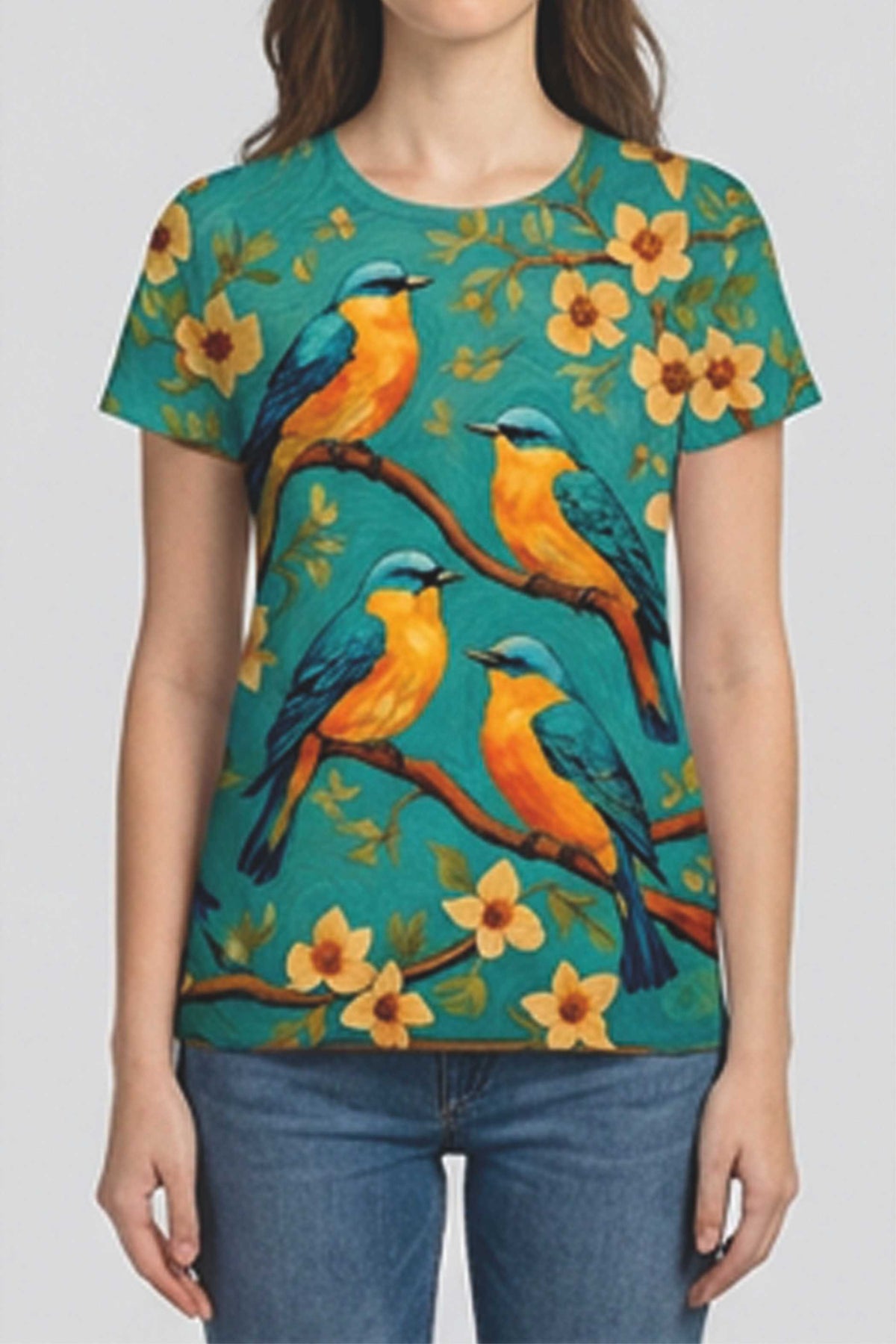 A woman wearing a short-sleeve crewneck t-shirt with a vibrant print of bluebirds perched on branches with yellow flowers against a teal background, paired with blue jeans.